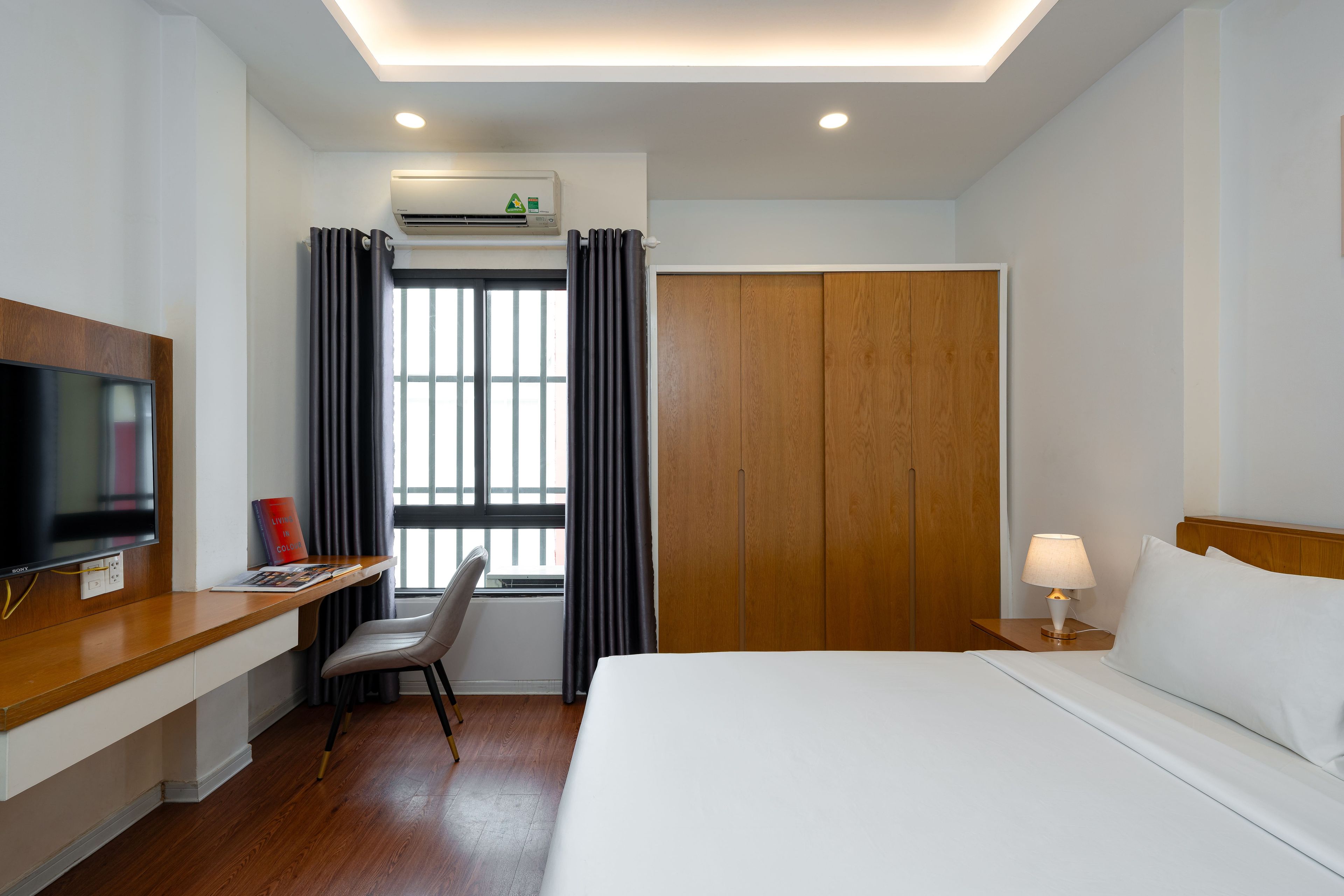 Ein Hotelzimmer mit Bett, Schreibtisch mit Fernseher, Stuhl, Kleiderschrank und einem Fenster mit Vorhängen.