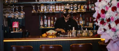 A bar with a bartender preparing drinks, shelves of liquor bottles, and bar stools.