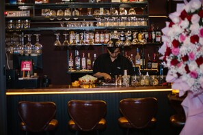Un bar avec un barman qui prépare des boissons, des étagères remplies de bouteilles d’alcool et des tabourets de bar.