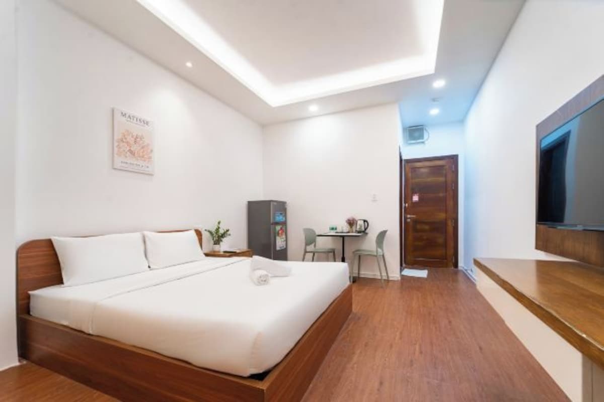 A hotel room with a wooden bed, a small desk, a television, and a wall-mounted artwork.