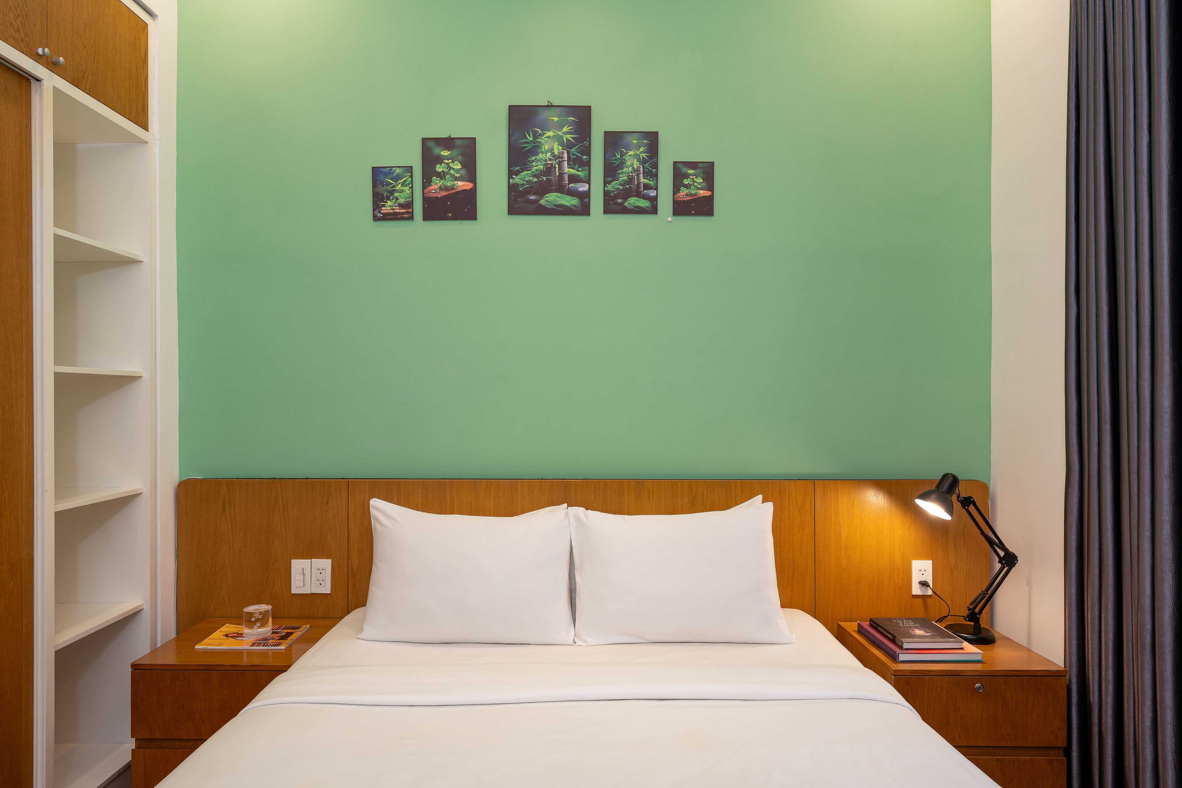 Een hotelkamer met een bed, nachtkastje, lamp en een muur met kunstwerk.