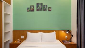 Habitación de hotel con cama, mesita de noche, lámpara y una pared decorada con obras de arte.