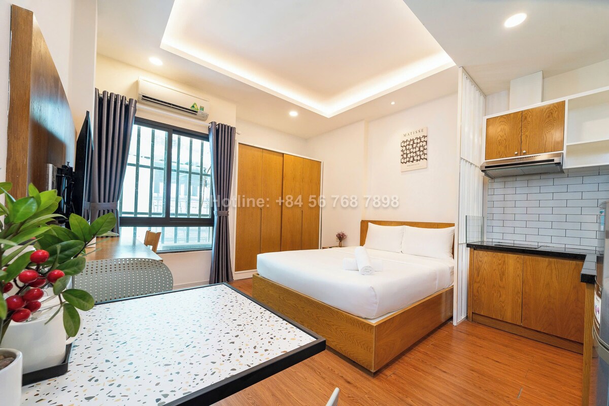 Une chambre d’hôtel moderne équipée d’un lit, d’une petite kitchenette, d’un coin repas et d’une grande fenêtre avec des rideaux.