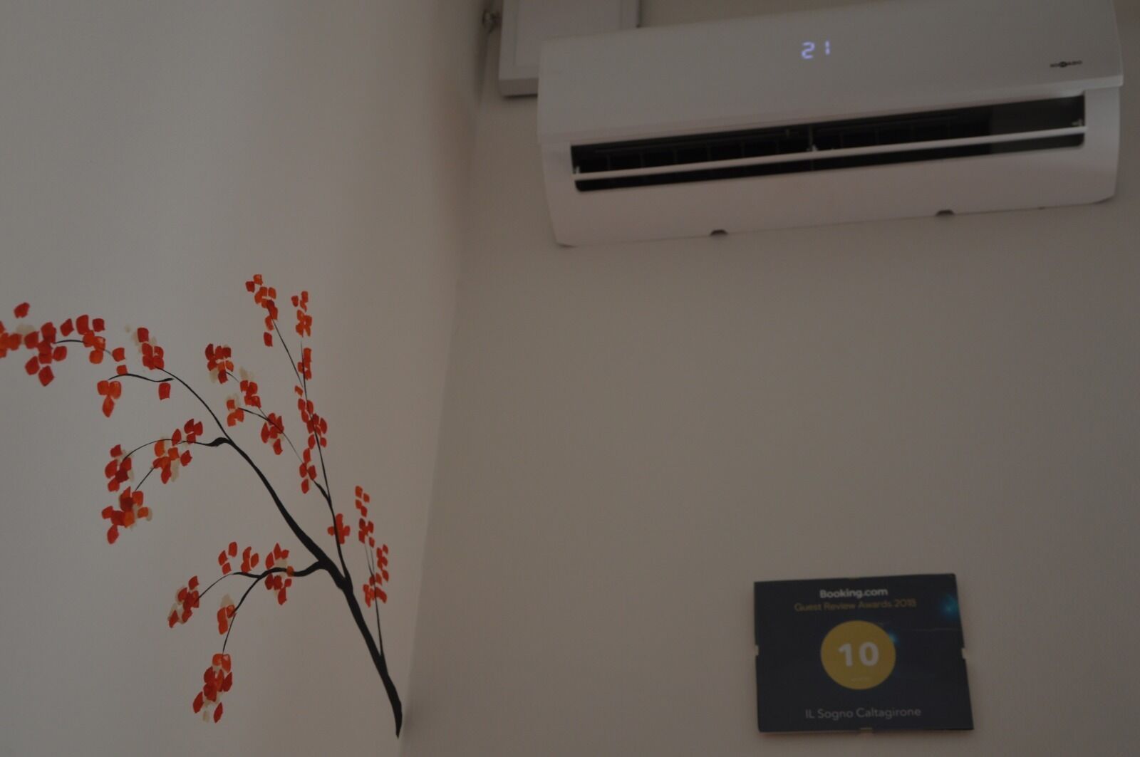 A wall with a red and black branch decoration, a thermostat set to 21 degrees, and a plaque indicating a guest award.