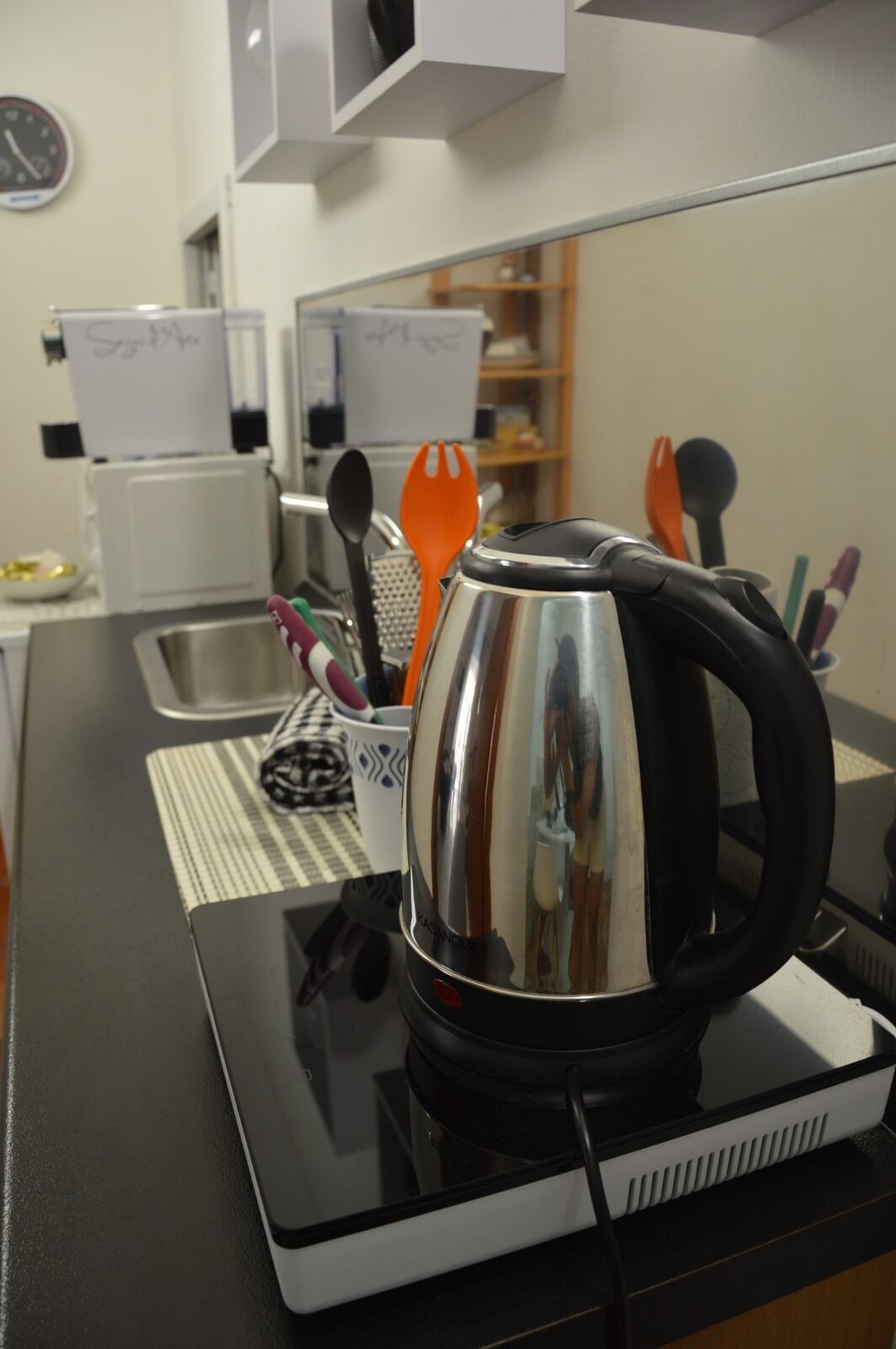 A kitchen area with a kettle on a countertop, a sink, and various utensils.