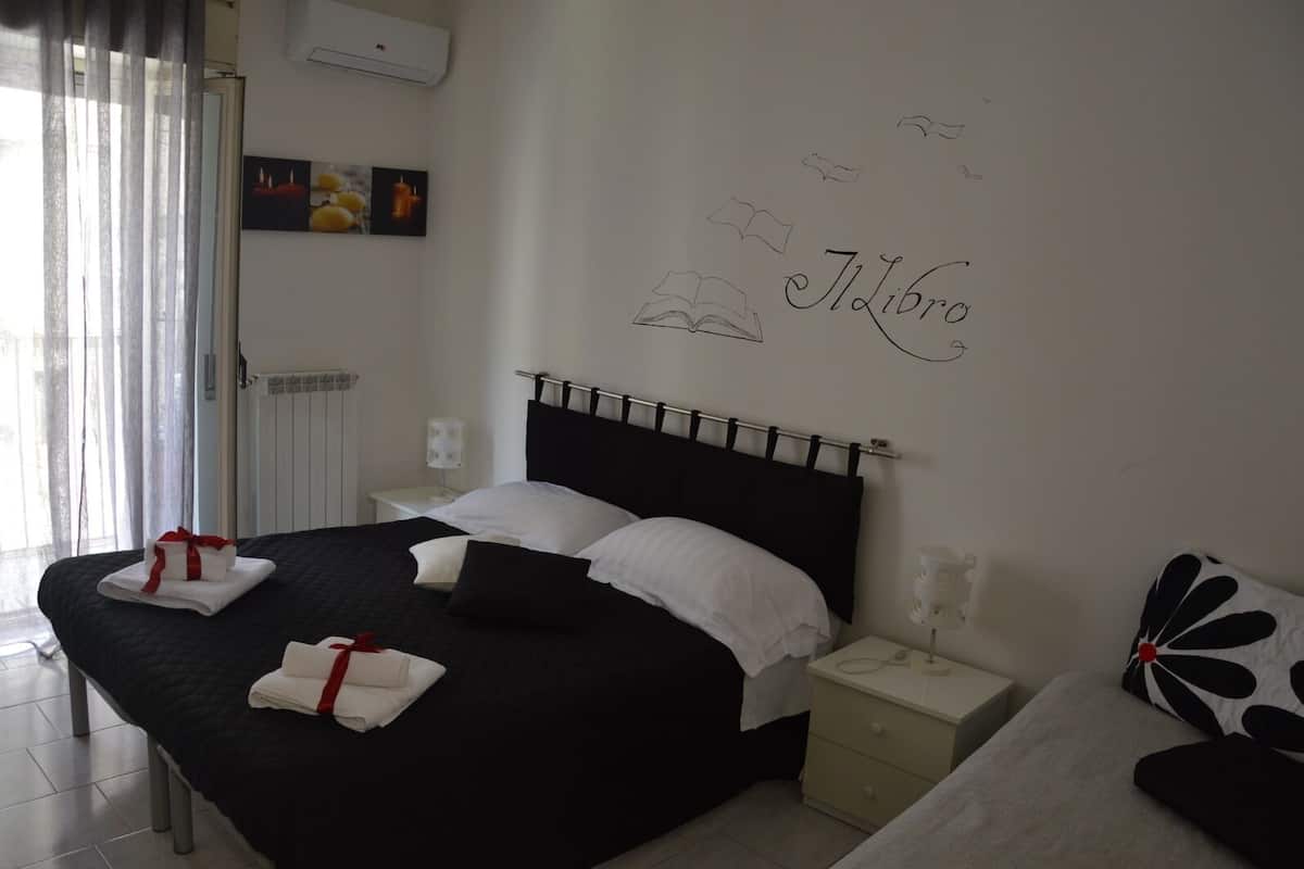 A neatly made bed with white and black bedding, a bedside table with a lamp, and a wall with a 'Il Libro' sign.
