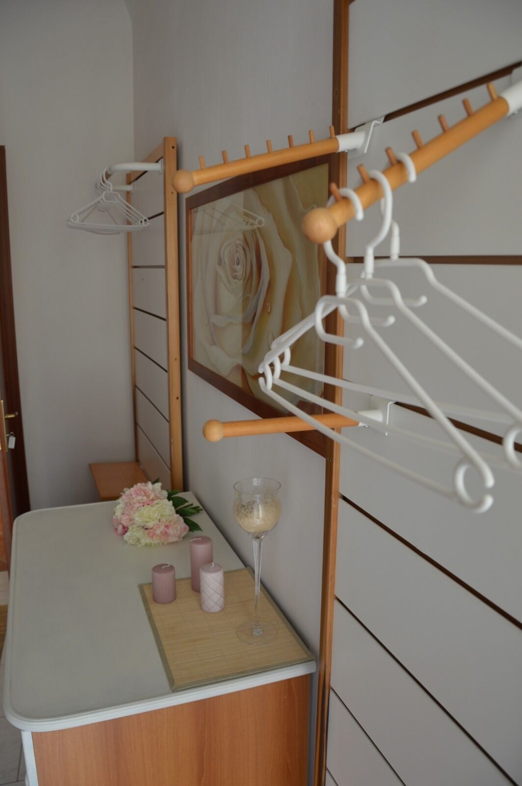 Quarto com estrutura de cama de madeira, mesa de cabeceira branca, espelho e um cabideiro.
