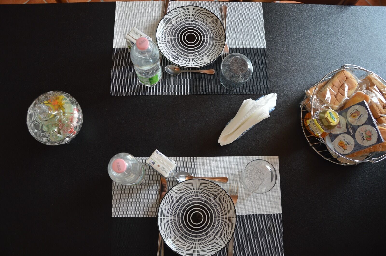 Een gedekte tafel met borden, kommen, een fles, een glas en een mand met brood.