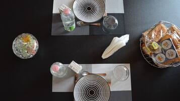 Een gedekte tafel met borden, kommen, een fles, een glas en een mand met brood.