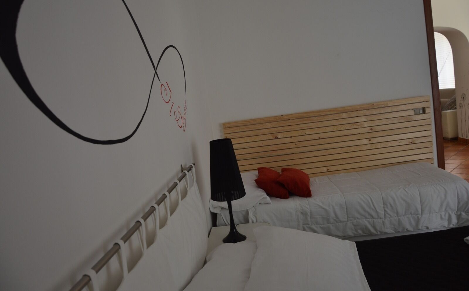 Een slaapkamer met een houten hoofdbord, een witte spreidekking, een rood kussen en een zwarte lamp op een nachtkastje.