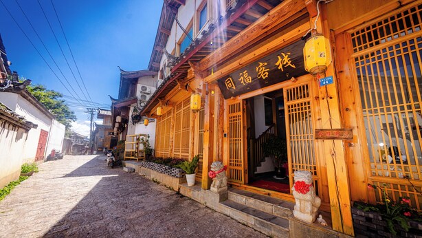 A traditional building with a wooden facade, a sign with Chinese characters, and a stone lion statue at the entrance. - Lijiang Tongfu Inn (Lijiang)