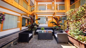 A spacious indoor courtyard with wicker furniture, potted plants, and a wooden balcony. - Lijiang Tongfu Inn (Lijiang)