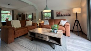 A cozy living room with two brown sofas, a wooden coffee table, and a floor lamp. - The Molshoop - Detached nature cottage in the middle of the Forest (IJhorst)