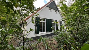 A white house with green shutters and a red-tiled roof, surrounded by dense foliage. - The Molshoop - Detached nature cottage in the middle of the Forest (IJhorst)