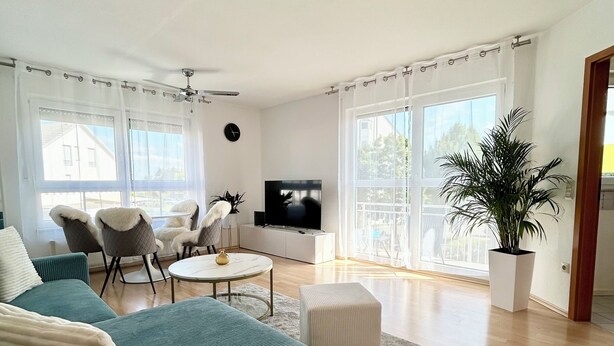 A modern living room with a teal sofa, a white ottoman, a round coffee table, and a TV on a white cabinet. - Sun oasis in Sigmaringen (Sigmaringen)