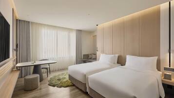 A hotel room with two beds, a dining table, a small round table, a bench, and a large window with curtains.