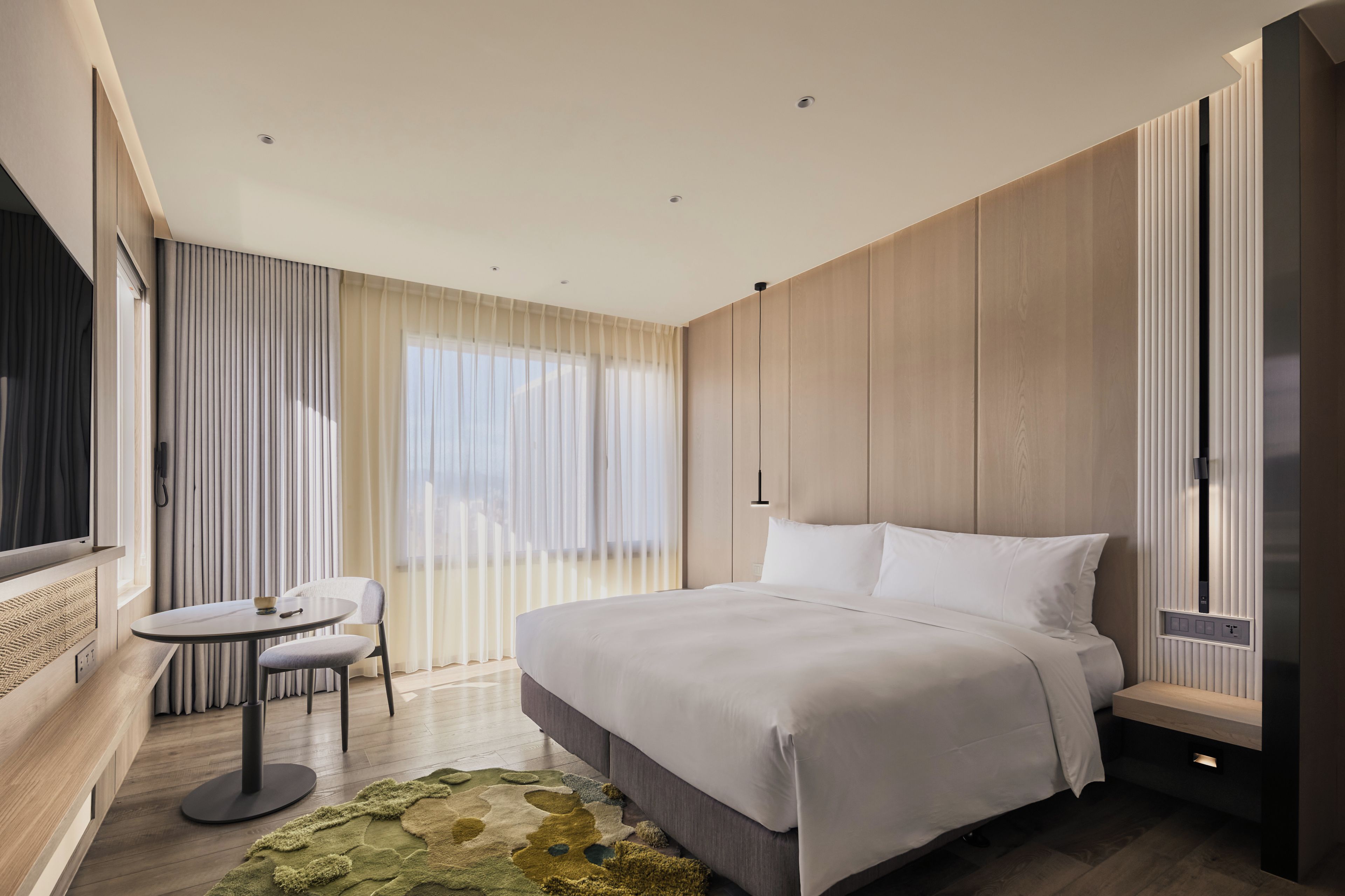 A modern hotel room with a large bed, a small round table, and a seating area.