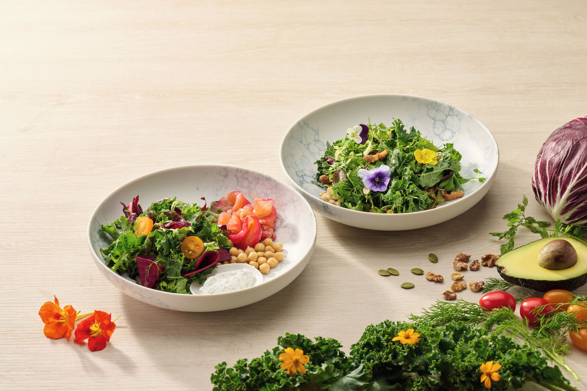 Dos ensaladas con diferentes verduras y frutos secos sobre una mesa de madera.