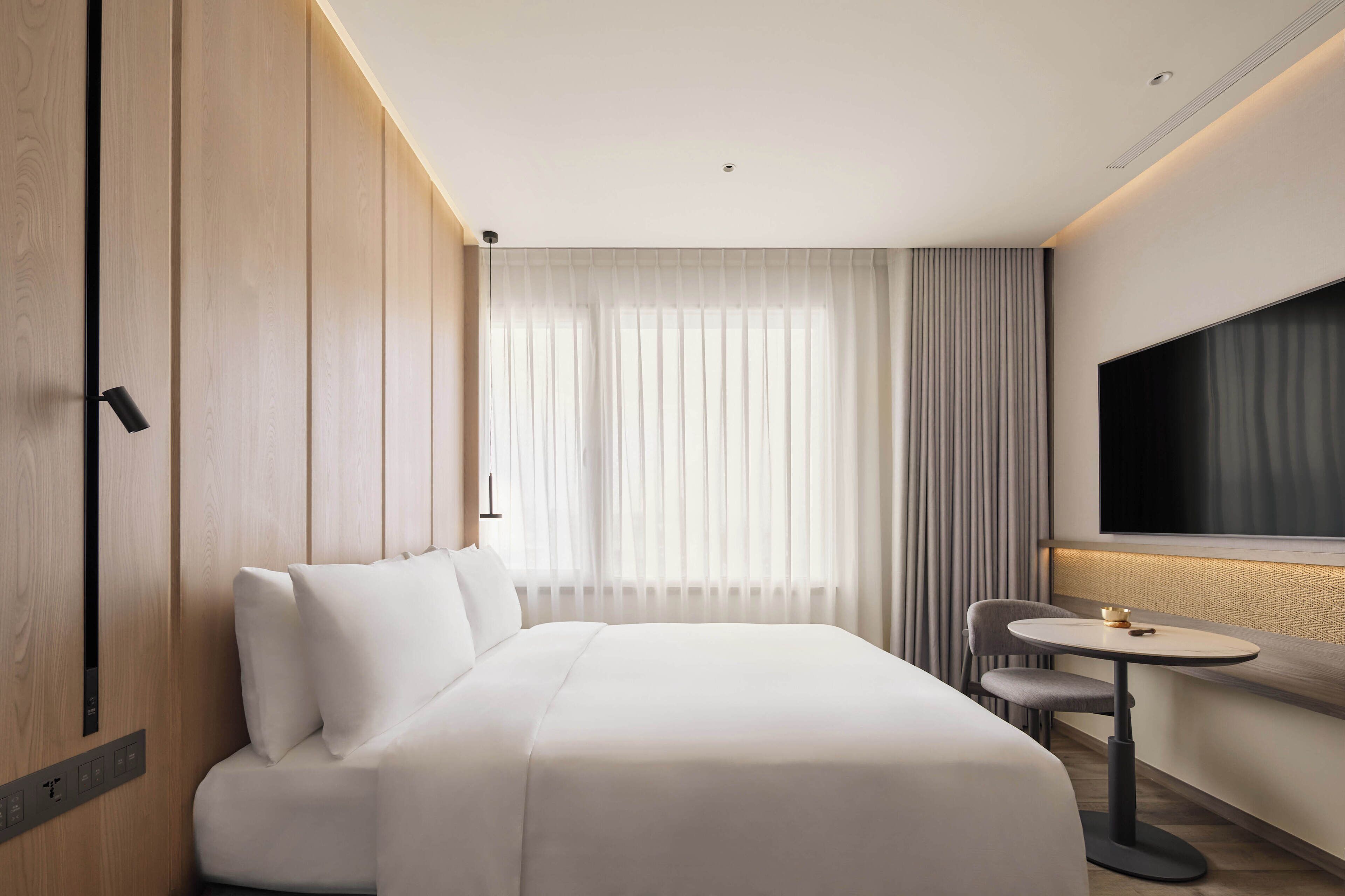 A modern hotel room with a large bed, a small table, a chair, and a TV.