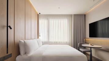 A modern hotel room with a large bed, a small table, a chair, and a TV.