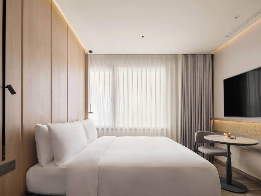 A modern hotel room with a large bed, a small table, a chair, and a TV.
