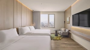 Una camera d'albergo con due letti, un divano, una televisione e vista sulla città.