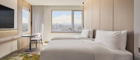 A hotel room with a large bed, a small table, a chair, a TV, and a window with a city view.