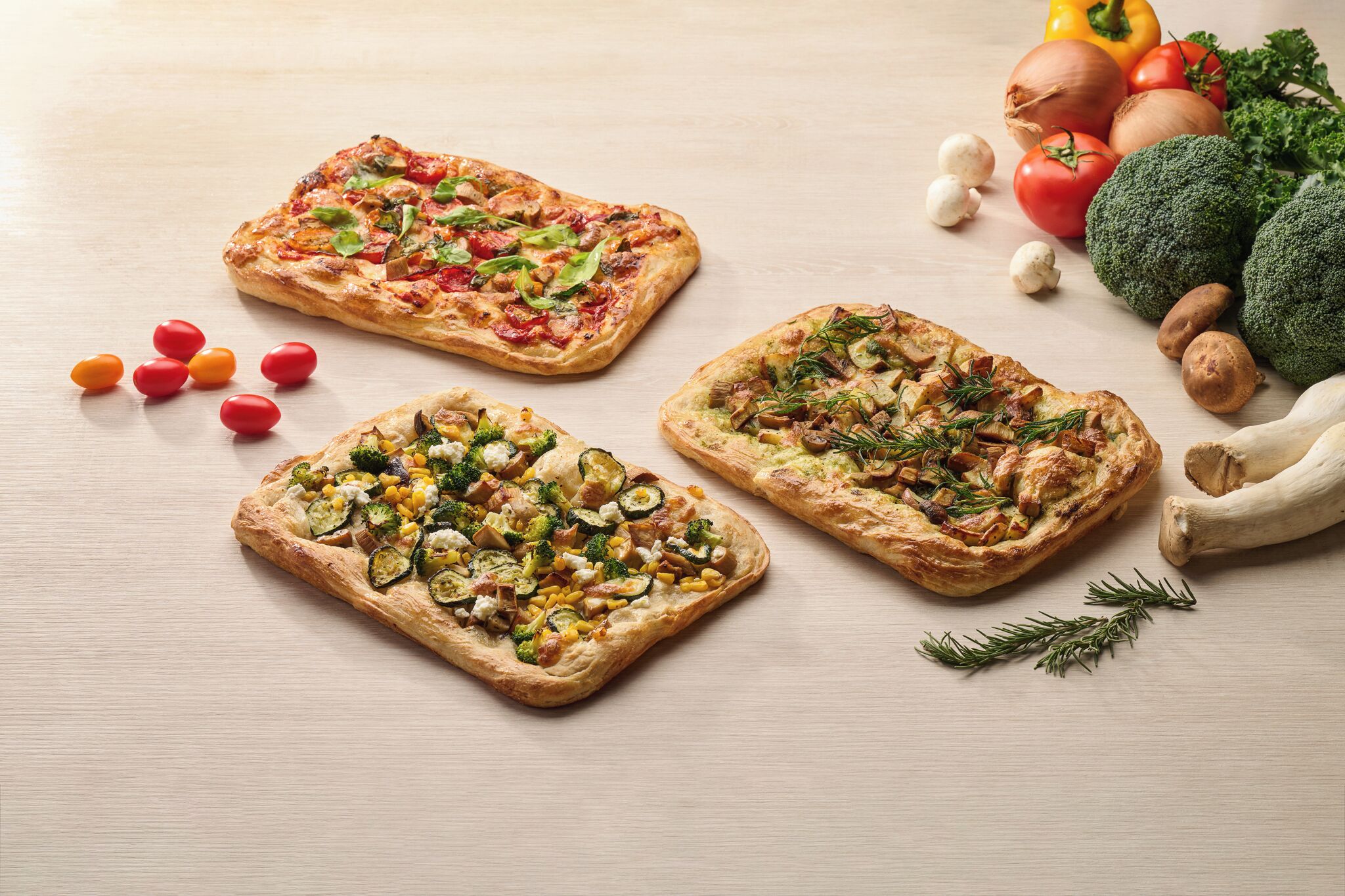 Drie pizza's met verschillende toppings op een houten tafel.