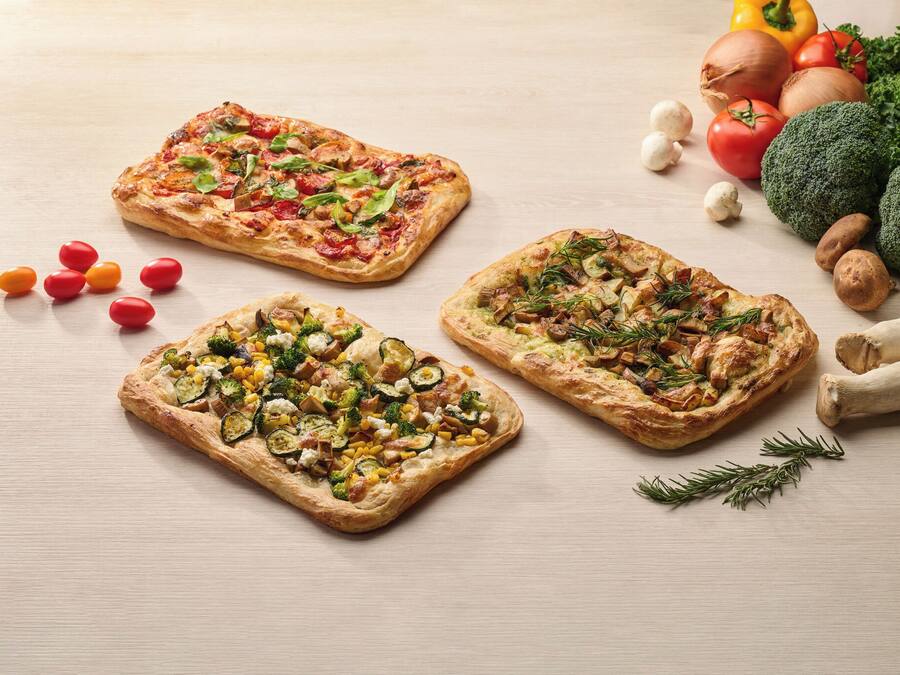 Drie pizza's met verschillende toppings op een houten tafel.