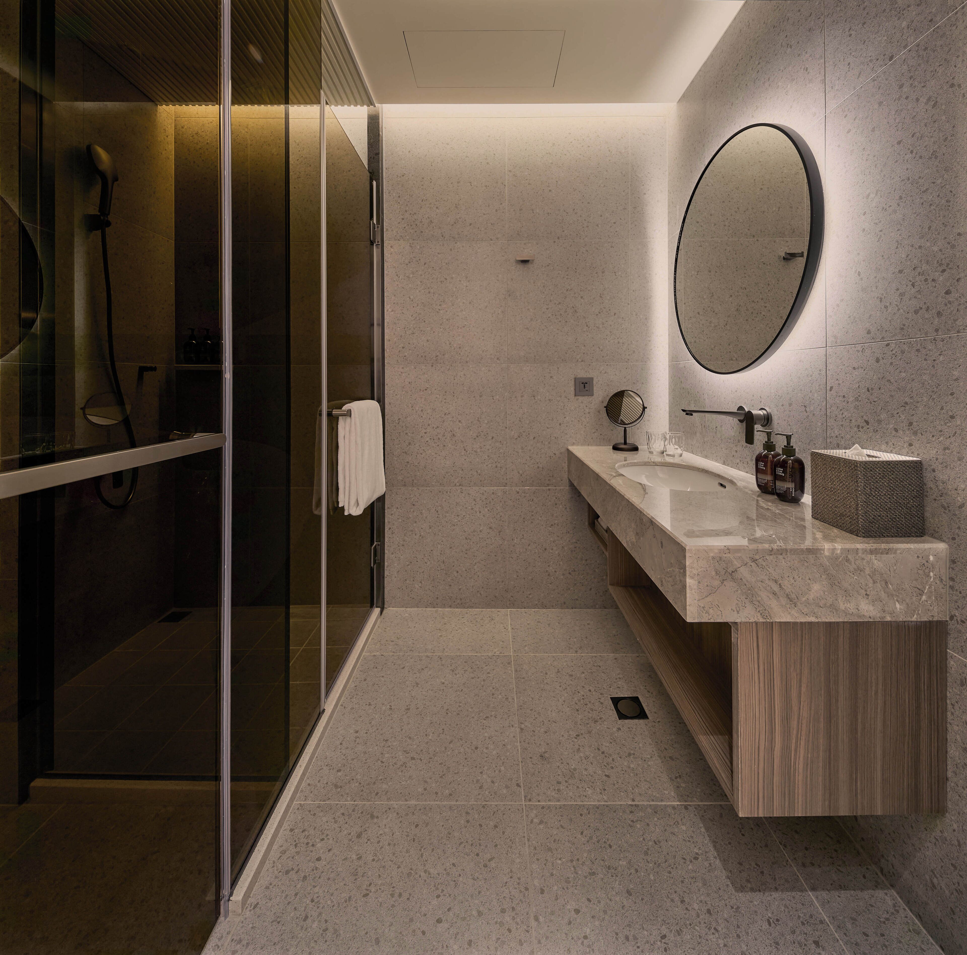 Un bagno moderno con box doccia in vetro, mobile lavabo in legno e uno specchio grande.