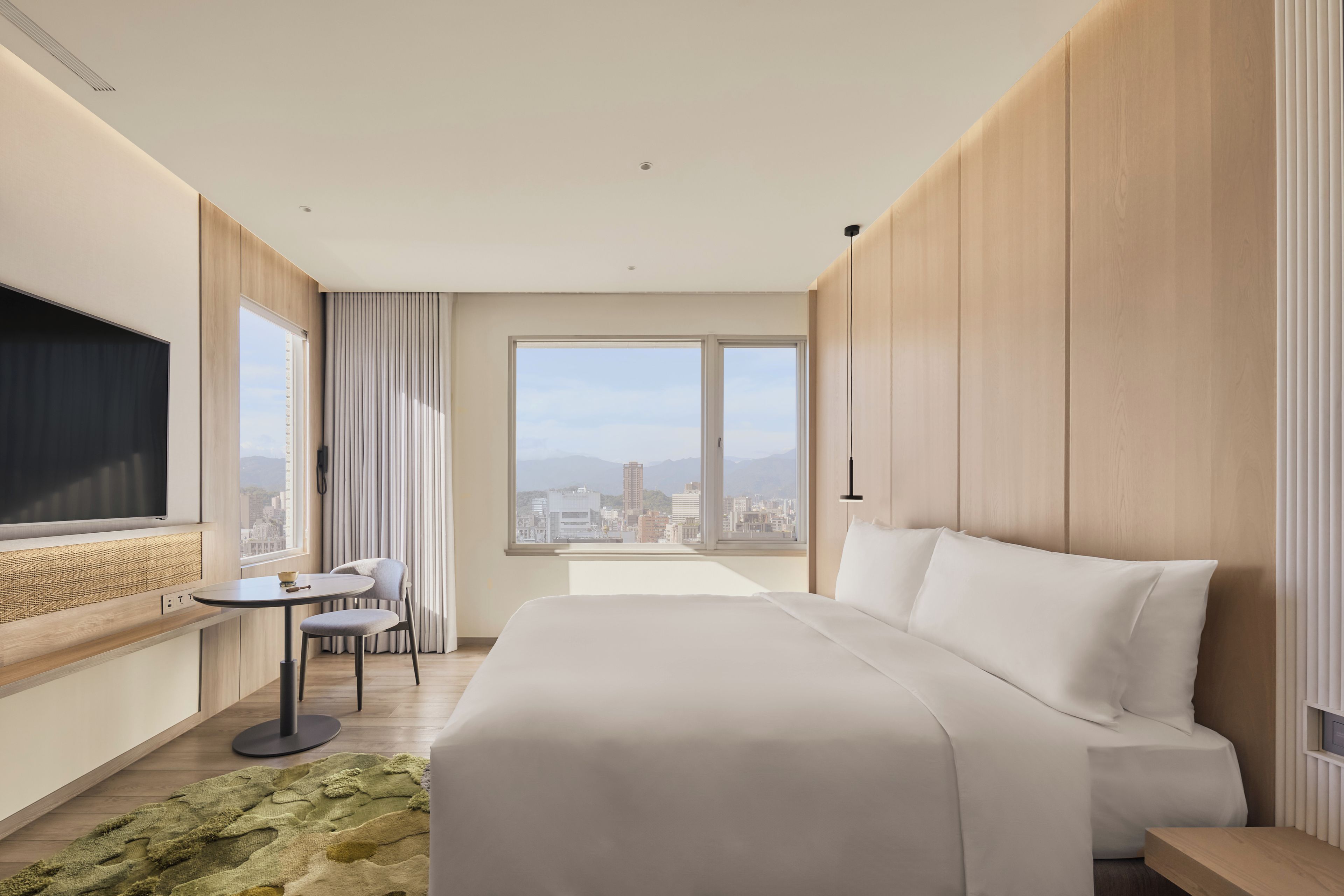 Habitació d'hotel moderna amb un llit gran, un escriptori i vista a un paisatge urbà per les finestres.