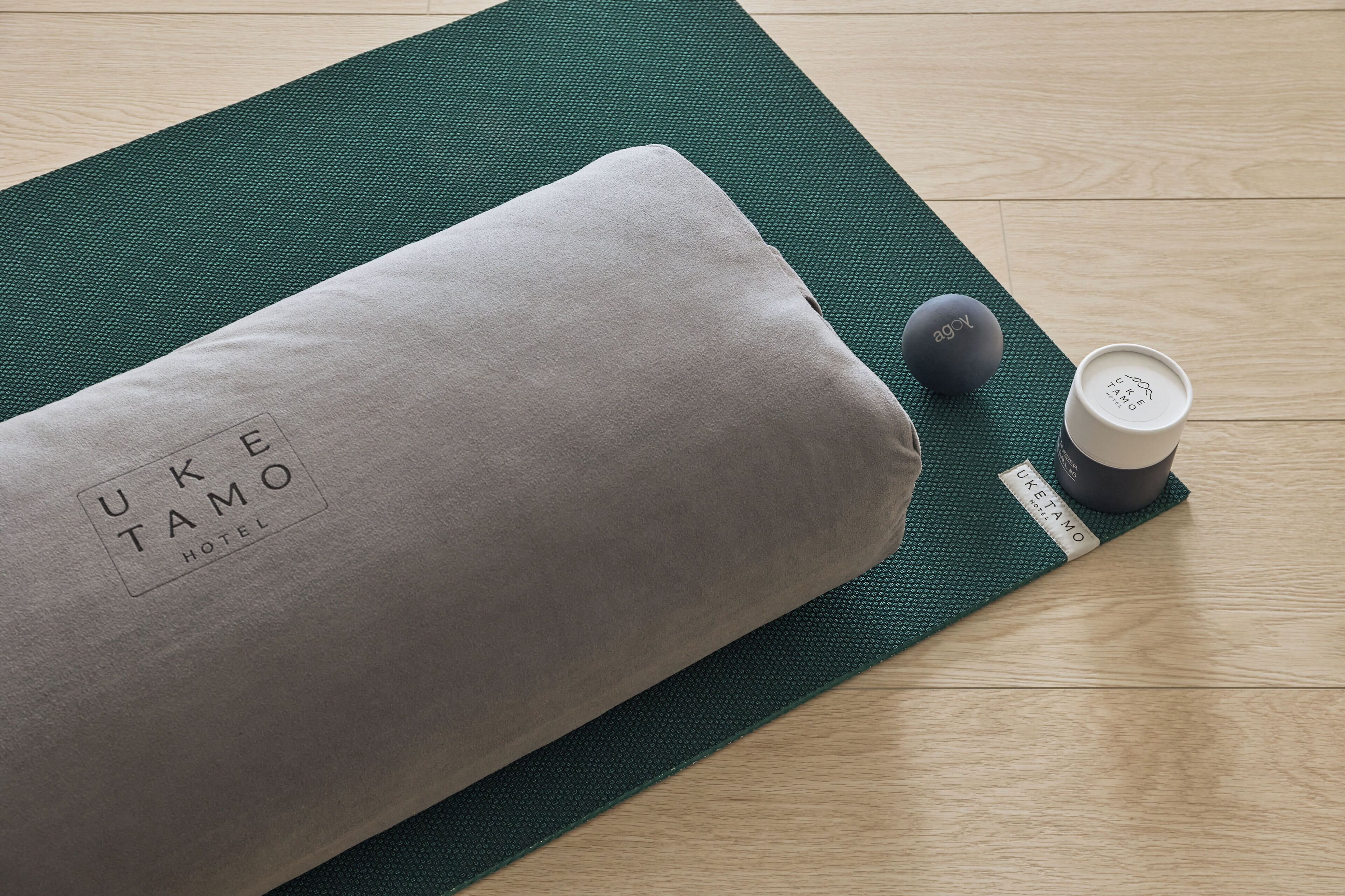A yoga mat with a grey cushion and a black object on a wooden floor.