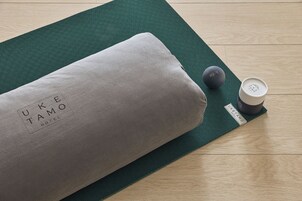 Una esterilla de yoga con un cojín gris y un objeto negro sobre un suelo de madera.