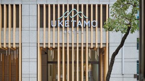 L'esterno dell'hotel Uketamo, dal design moderno, con un cartello ben visibile e un albero di fronte.