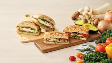 Tábua de madeira com vários sanduíches e vegetais frescos como tomates, pepinos e abacate.
