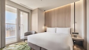 Camera d'albergo moderna con un ampio letto, un'area salotto e un balcone con vista sulla città.