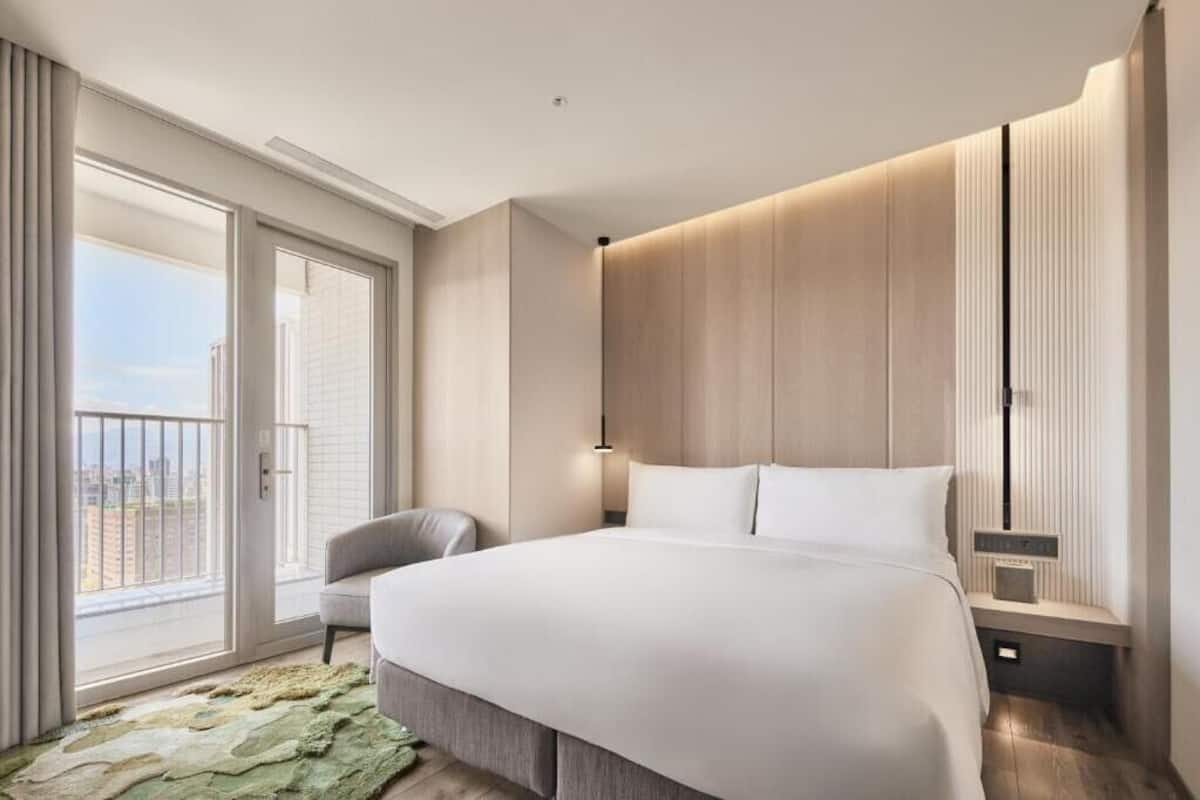 A modern hotel room with a large bed, a seating area, and a balcony with a city view.