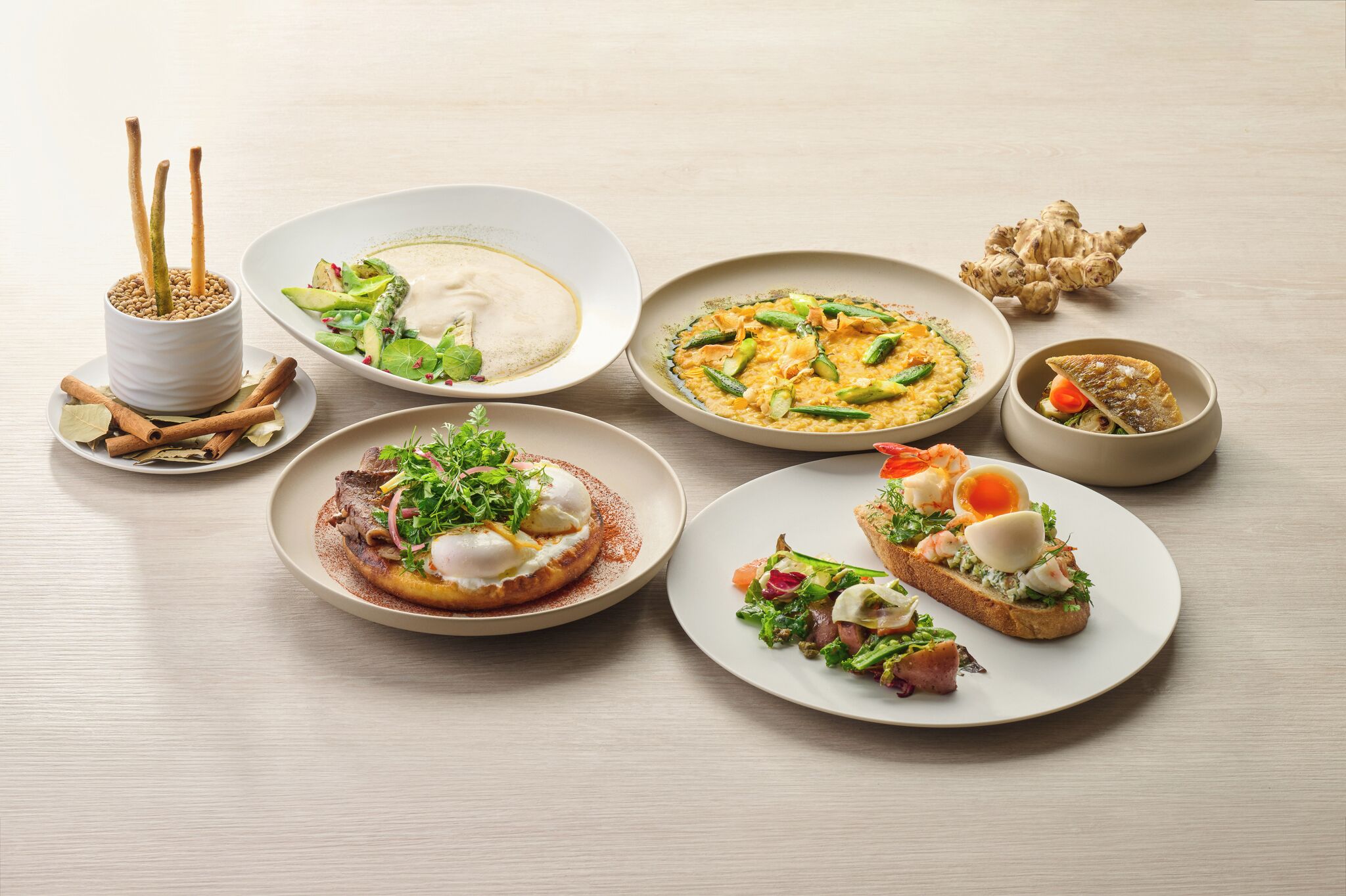 A variety of dishes on a table, including a poached egg on toast, a salad, and a bowl of soup.