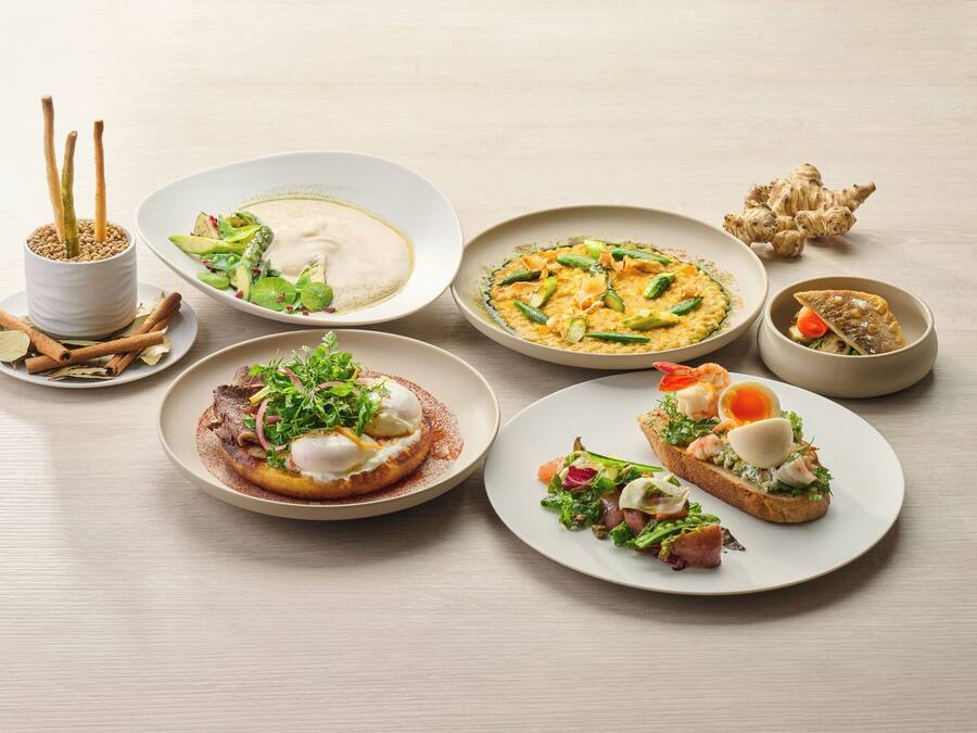 A variety of dishes on a table, including a poached egg on toast, a salad, and a bowl of soup.