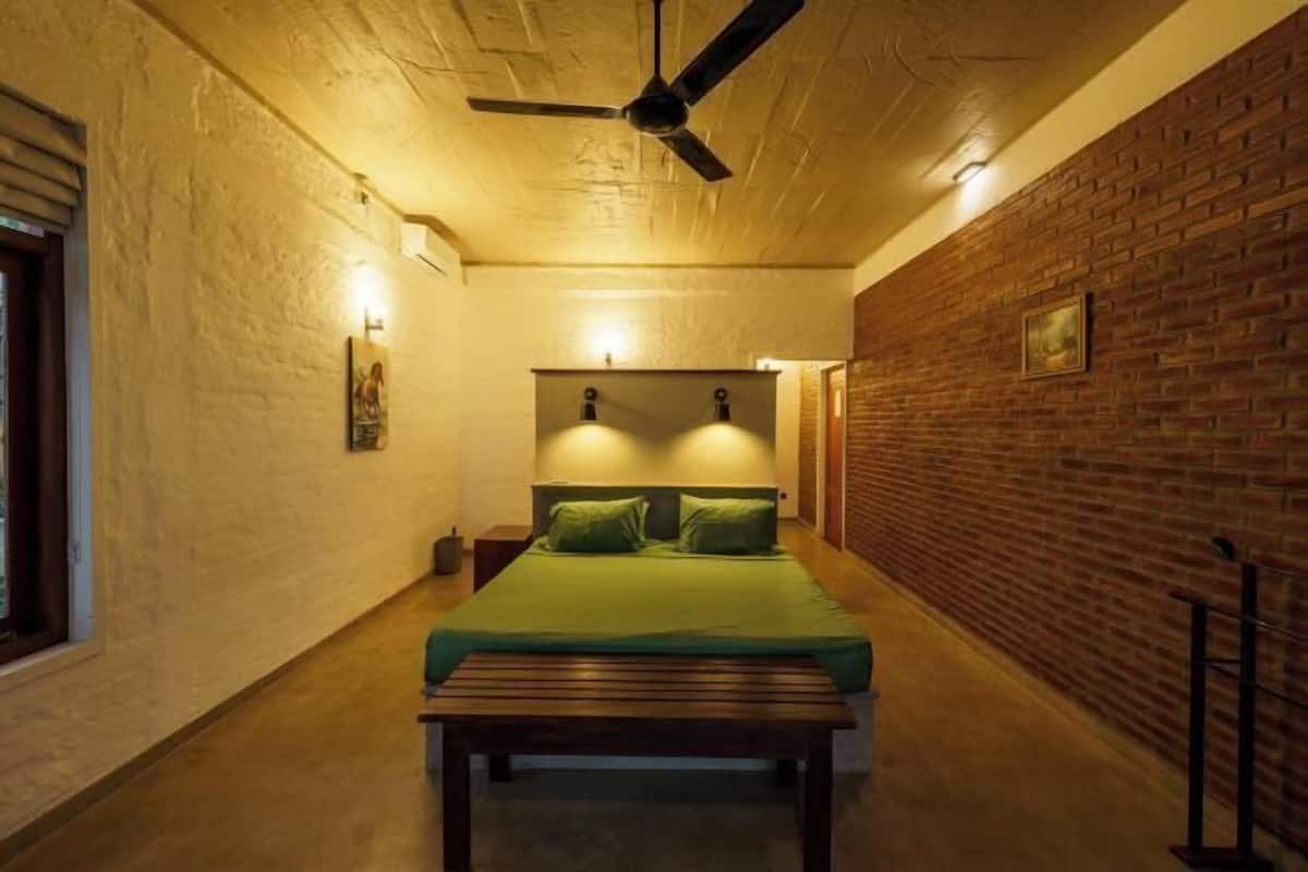Un couloir étroit mène à une pièce qui contient un lit, un ventilateur de plafond et un mur en briques.