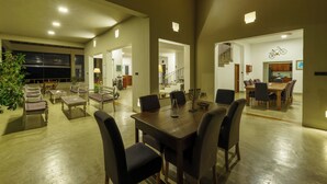 Un vaste espace de salle à manger avec une grande table en bois et de nombreuses chaises, attenant à une cuisine et à un salon, auquel on accède par un escalier.