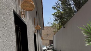 Un callejón estrecho con un edificio blanco, un coche blanco al final y una palmera a la derecha.