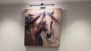 Una habitación con una mesa redonda, dos sillas grises, un tapete tejido y un cuadro abstracto grande en la pared.
