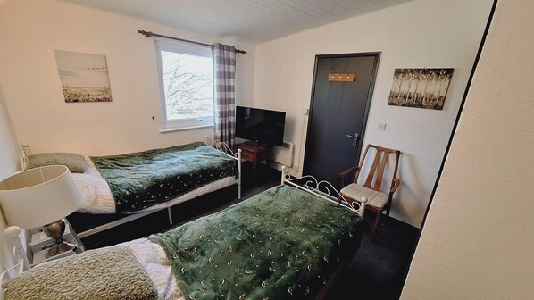 A room with two single beds, a television, a door, and a window with curtains.