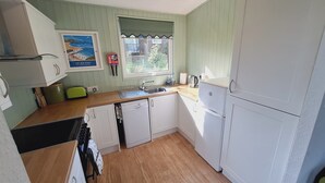 Une cuisine compacte avec des meubles blancs, un plan de travail en bois, un lave-vaisselle encastré et une fenêtre donnant sur le jardin.