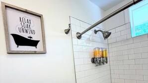 A modern bathroom with a shower, a framed sign saying "RELAX SOAK UNWIND", and a towel rack with a white towel. - Renovated 2 Bedroom  in Durham!  New listing but experienced Superhost! (Durham)