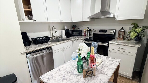 A modern kitchen with white cabinets, a stainless steel dishwasher, a black stove, and a marble countertop. - Renovated 2 Bedroom  in Durham!  New listing but experienced Superhost! (Durham)