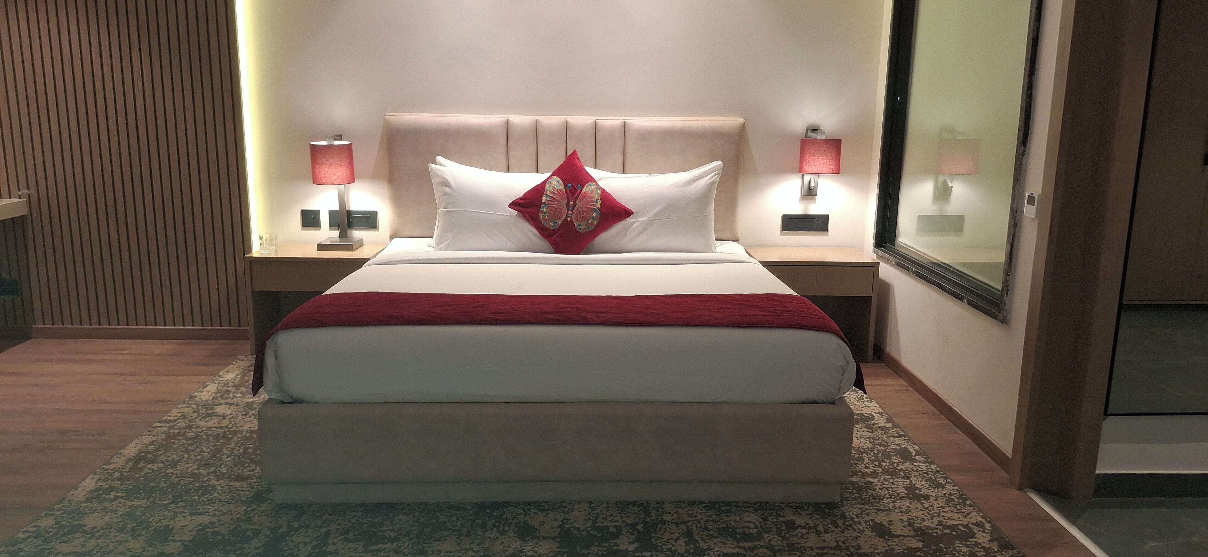 Habitación de hotel con una cama grande, dos mesitas de noche con lámparas, un panel de pared de madera y un espejo amplio.