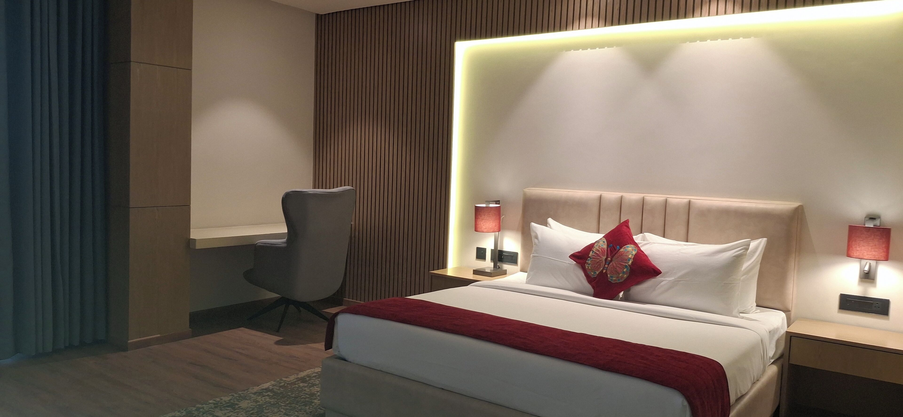 A modern hotel room with a bed, bedside lamps, a desk, and a chair.
