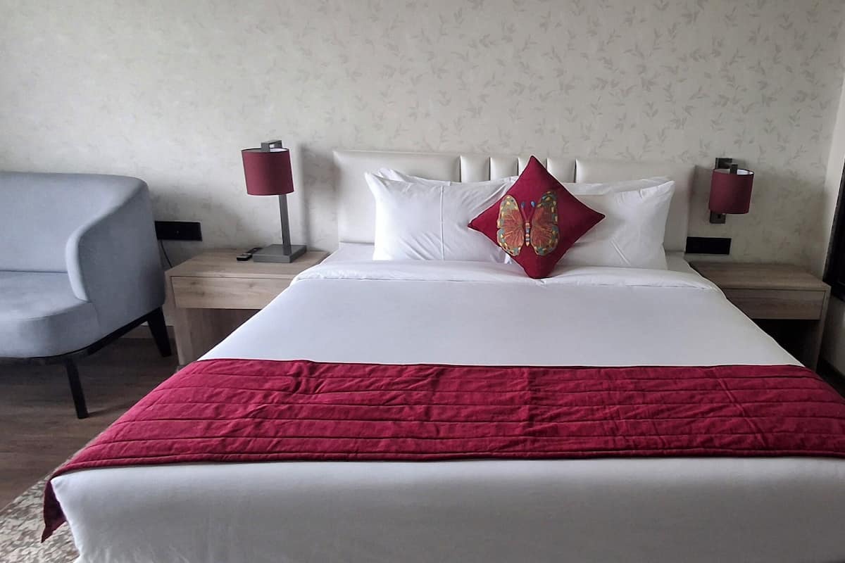 Ein Hotelzimmer mit einem großen Bett, einer roten Tagesdecke, zwei Nachttischlampen, einem Nachttisch, einem Stuhl und einem großen Fenster.